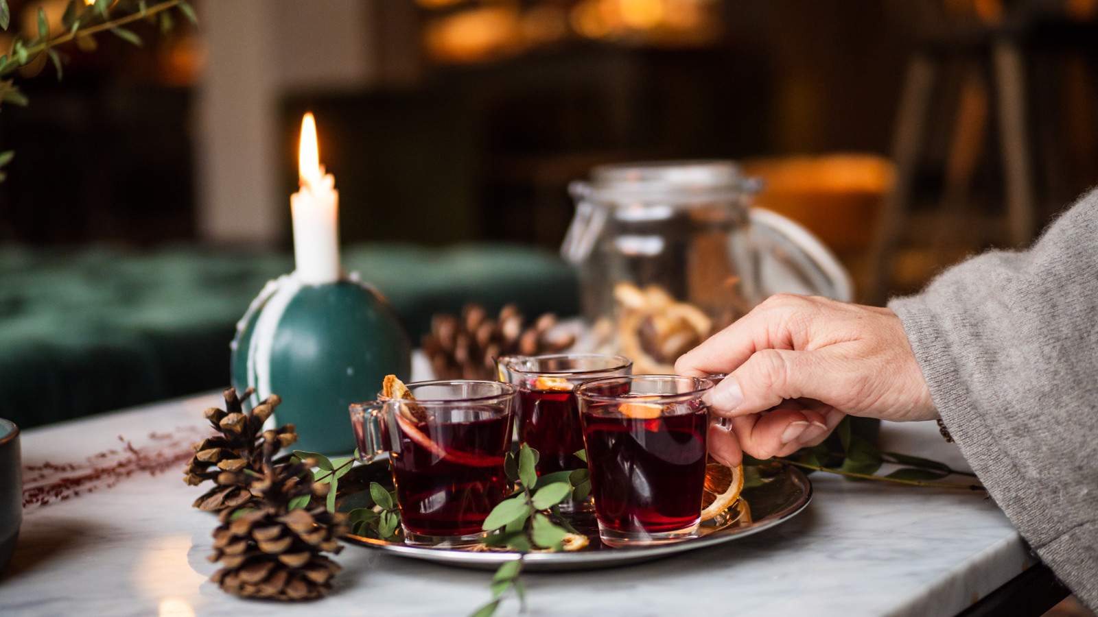 A hand reaching for a glass of mulled wine standing on a golden tray