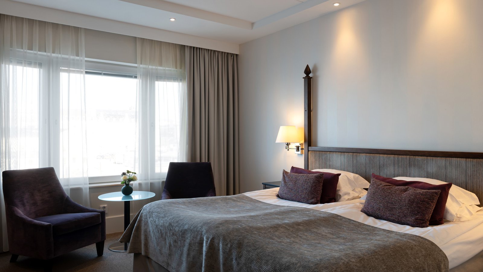 Hotellsäng med silvrigt överkast och lila kuddar