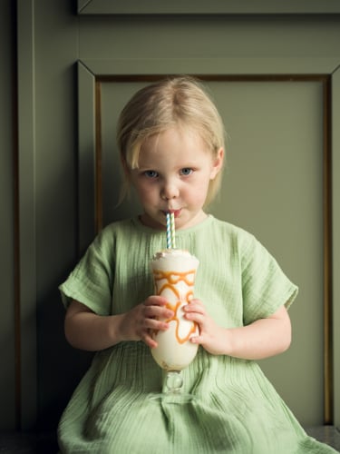 Flicka i grön klänning som dricker milkshake med sugrör