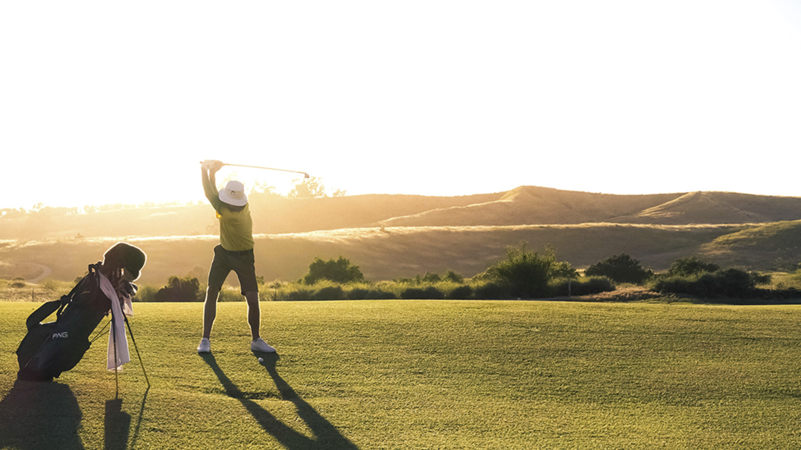 Golfspelare som svingar en klubba i solnedgången