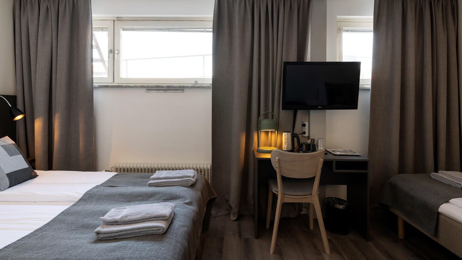 Ljust hotellrum med två enkelsängar med sänggavel i trä, tv, fönster och gardiner