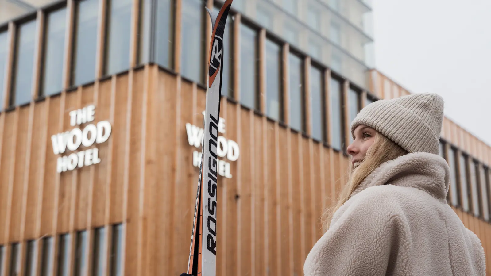 Skidåkare hållandes i ett par längdskidor som står framför The Wood Hotel by Elite