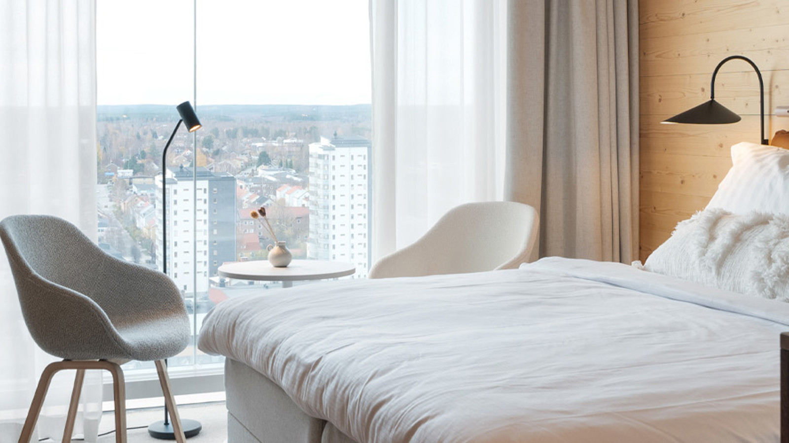 Mysigt hotellrum med dubbelsäng, tv, stolar och stora fönster med utsikt över Skellefteå