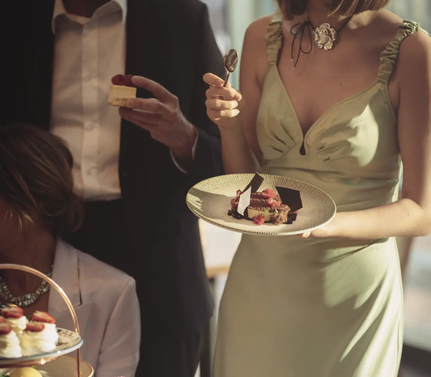 Elegant gathering with guests enjoying a variety of desserts, including a chocolate cake and a tiered stand of pastries topped with strawberries.