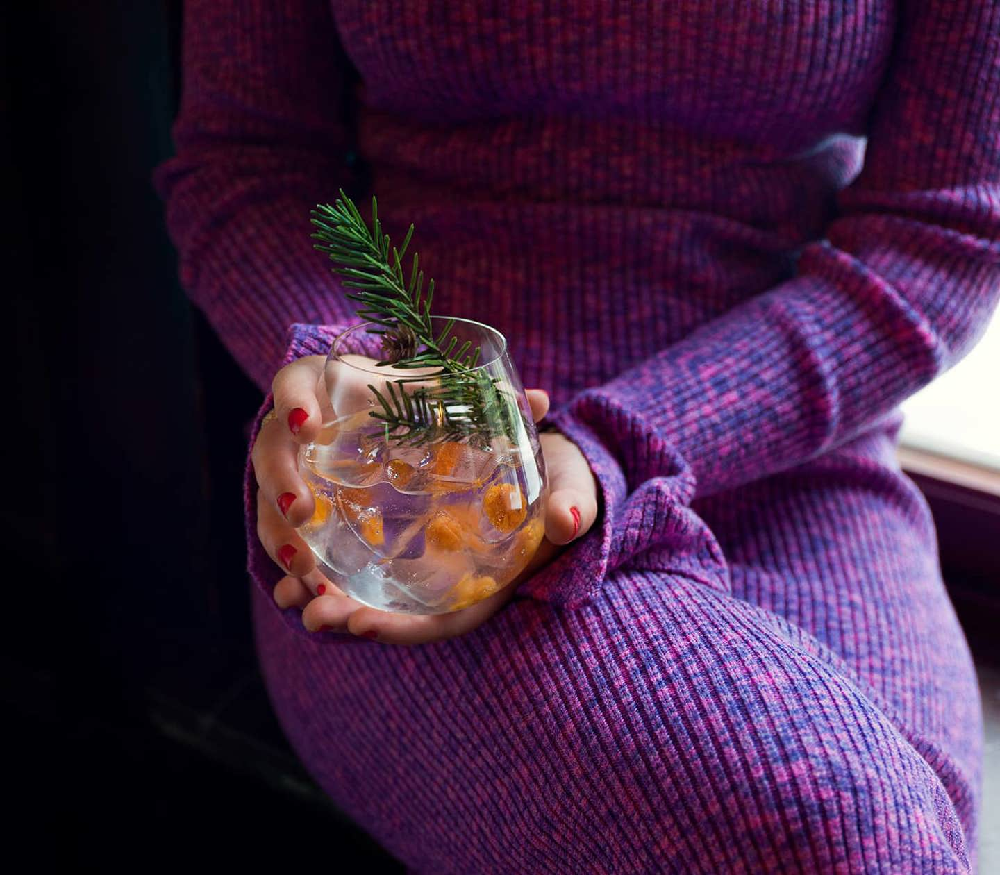 Bild på en drink med granskott hållandes av kvinna i lila klänning