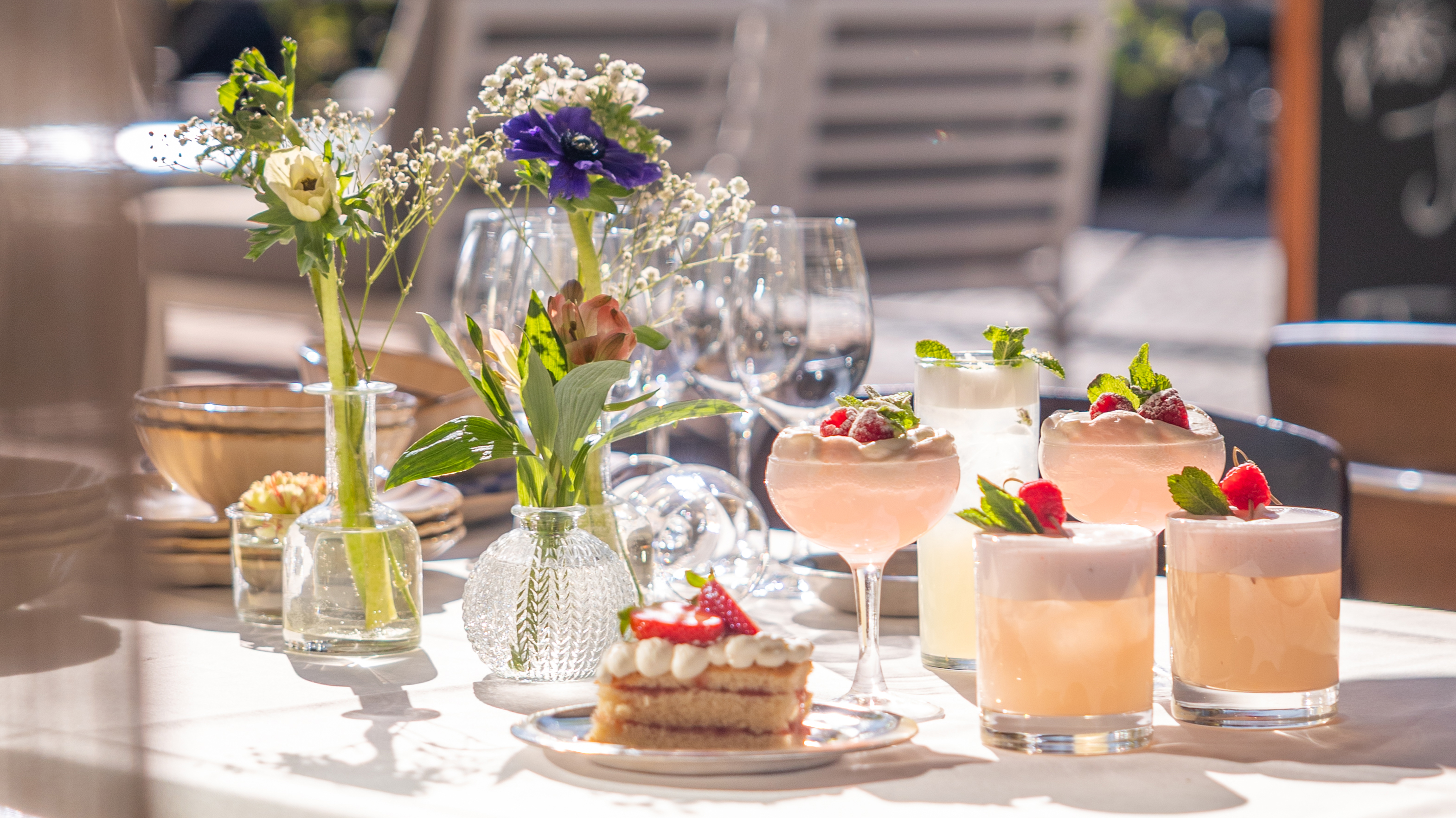 Somrigt bord med blommor, tårta och drinkar