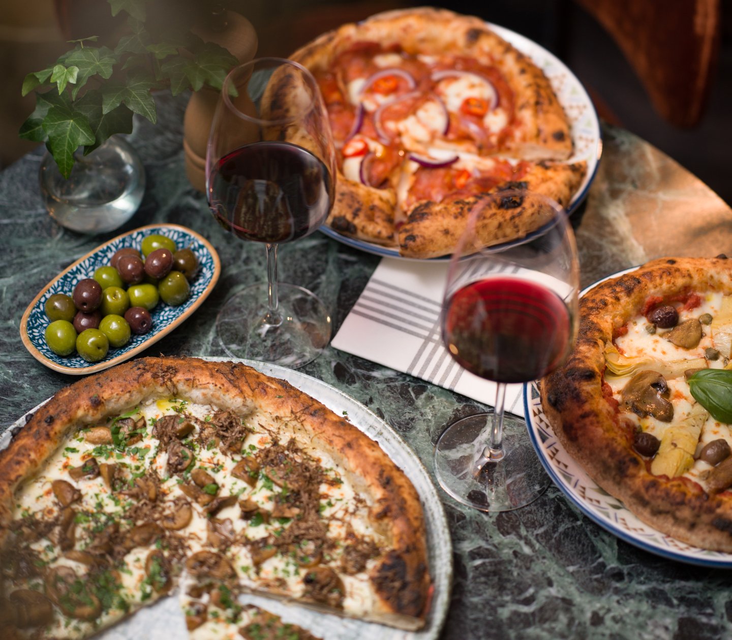 Bord med olika pizzor, oliver och vinglas med rödvin