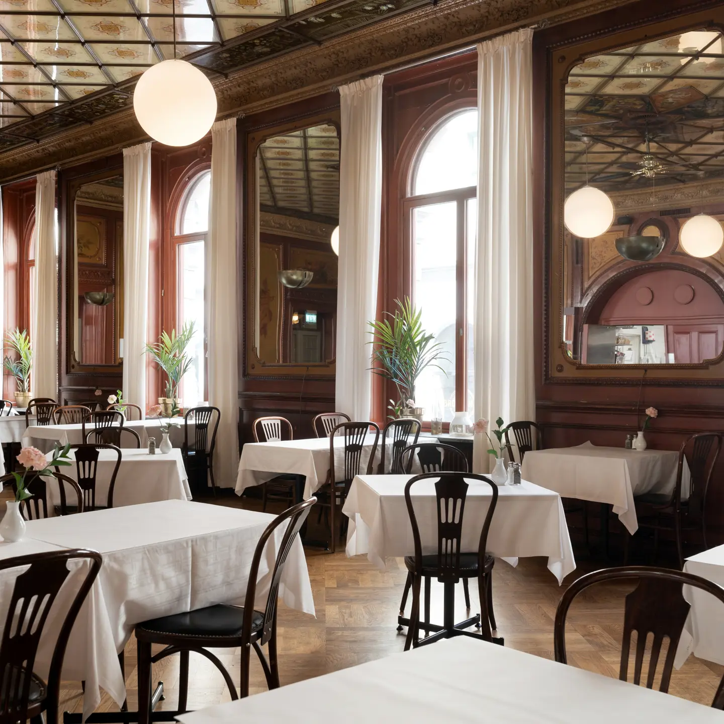 Nice dining room with mirrors on the walls and ceiling with large windows, many tables and chairs with white tablecloths