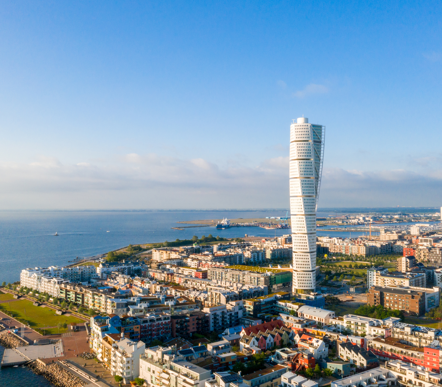 Aerial view of a modern twisted skyscraper in coastal Malmö with clear blue sky.