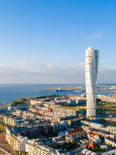 Aerial view of a twisting skyscraper in a modern cityscape during golden hour with river and harbor in the background.