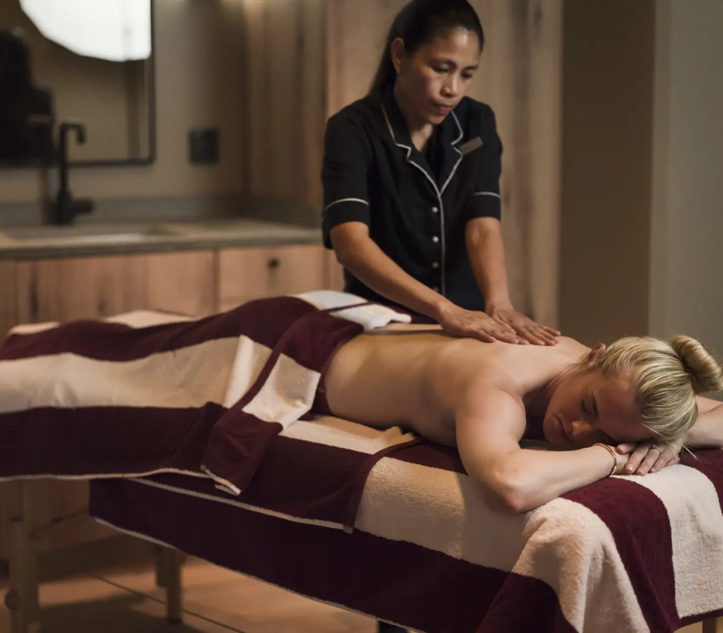 En person får ryggmassage på ett spa, terapeut i svart uniform, avslappnande atmosfär