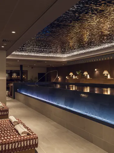 Inomhus spa med uppvärmd pool, omgiven av eleganta vilstolar och stämningsfull belysning, skapar en avkopplande atmosfär.