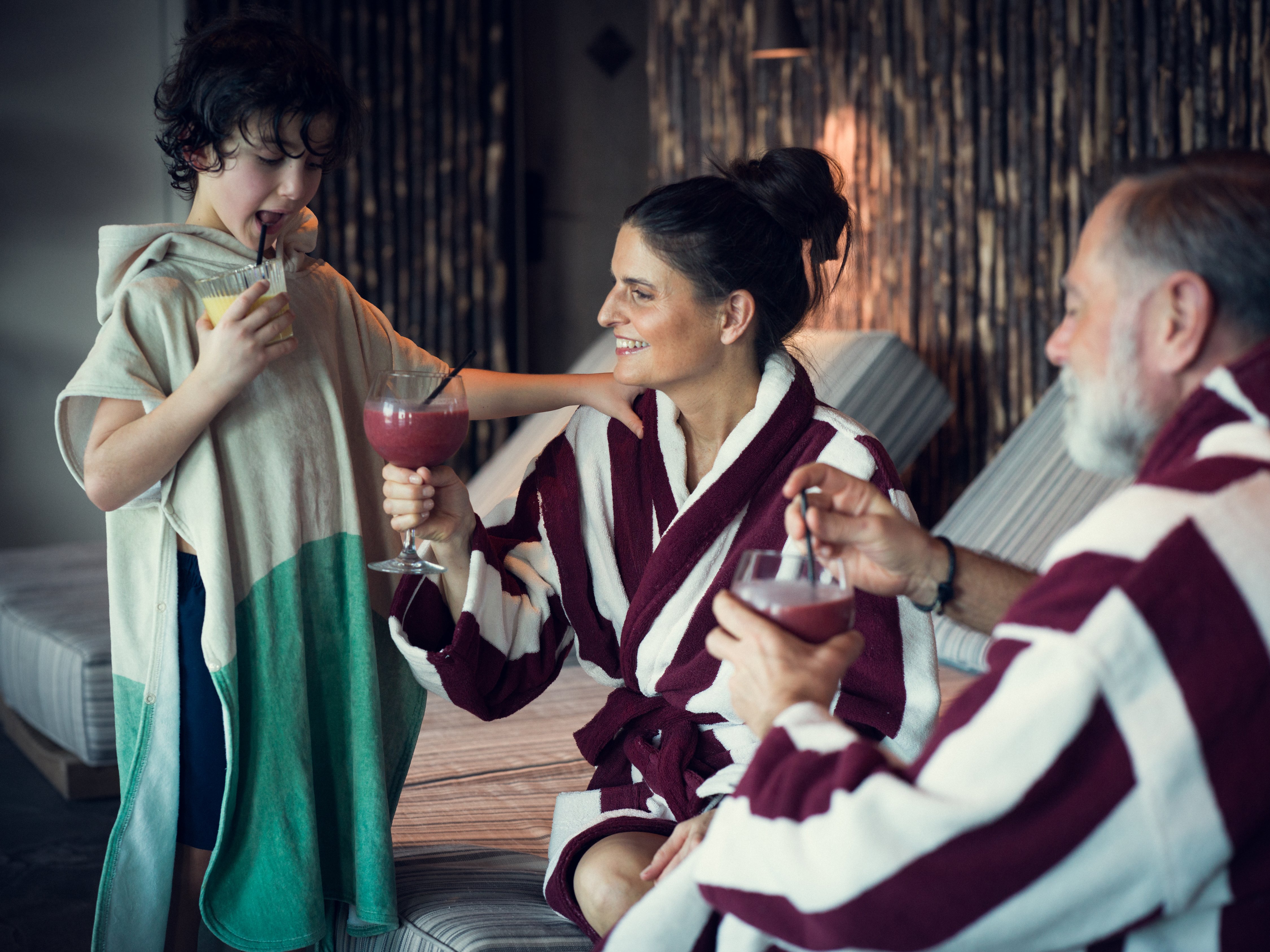 Två vuxna i badrockar och pojke i poncho på spa 