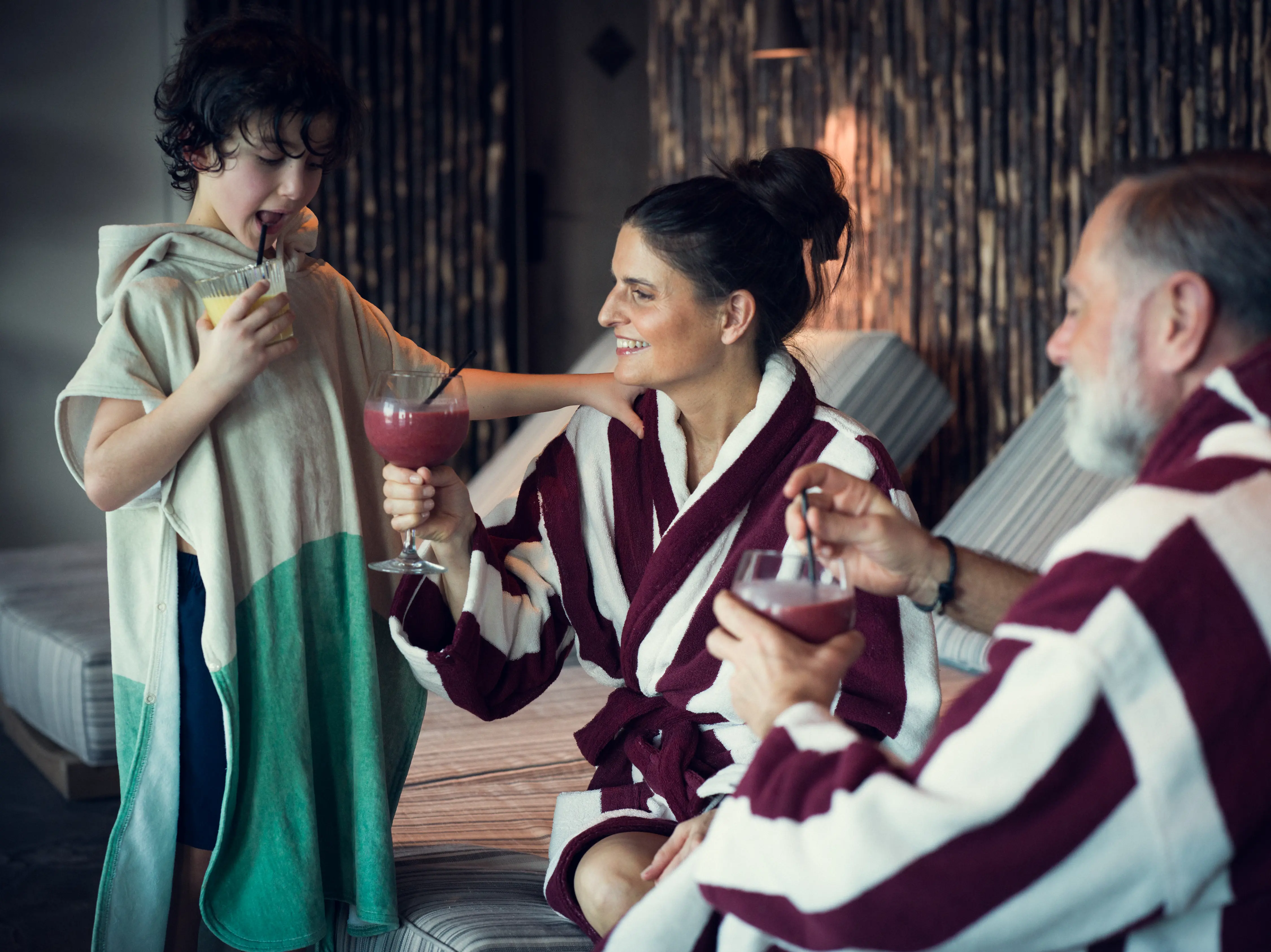 Family enjoying drinks together at a spa, wearing matching maroon and white robes, with a relaxing atmosphere.